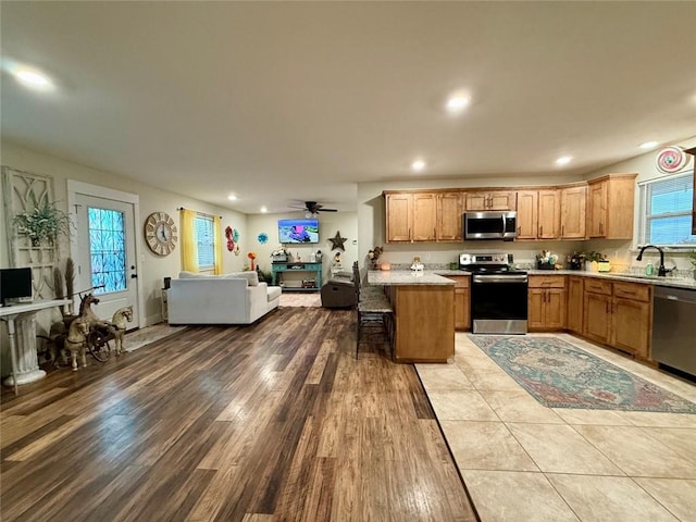 kitchen with appliances with stainless steel finishes, hardwood / wood-style floors, sink, a breakfast bar area, and ceiling fan