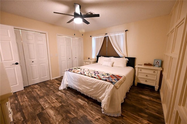 bedroom featuring dark wood-type flooring, two closets, a textured ceiling, and ceiling fan