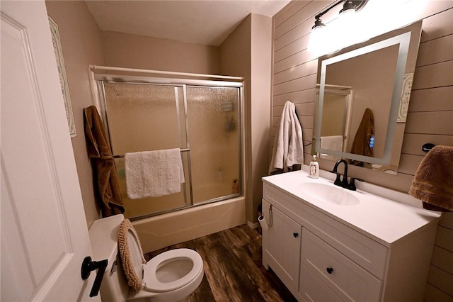 full bathroom featuring toilet, wood walls, wood-type flooring, shower / bath combination with glass door, and vanity