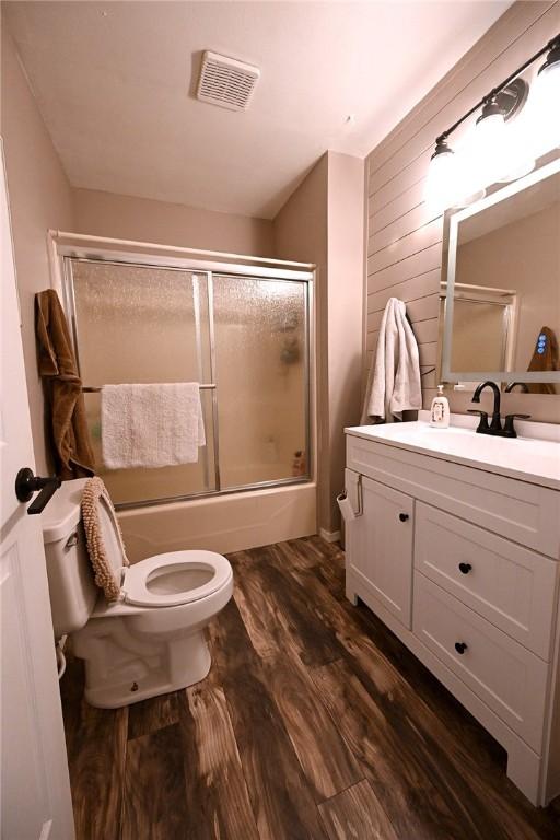 full bathroom featuring toilet, wood walls, bath / shower combo with glass door, vanity, and hardwood / wood-style flooring