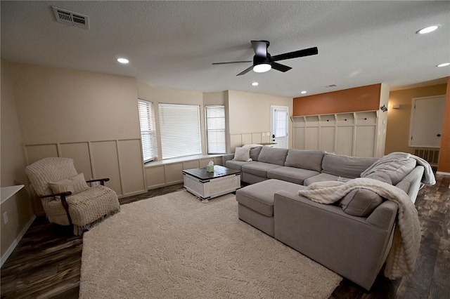 living room featuring dark wood-type flooring, ceiling fan, and a textured ceiling