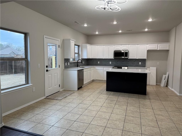 kitchen with appliances with stainless steel finishes, white cabinetry, a center island, light tile patterned flooring, and decorative backsplash