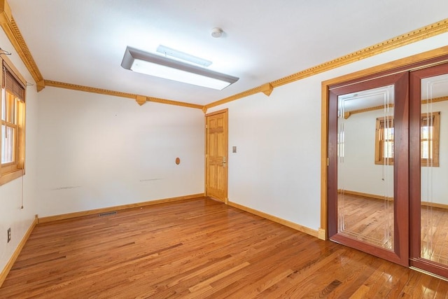 spare room with ornamental molding, light wood-style flooring, and baseboards