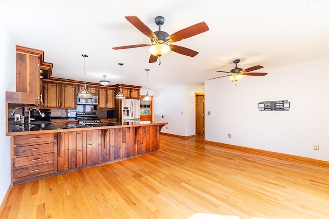 kitchen with stainless steel appliances, a peninsula, a sink, brown cabinets, and light wood finished floors