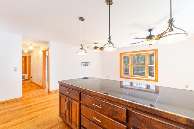 kitchen featuring tile counters, brown cabinets, hanging light fixtures, and light wood finished floors