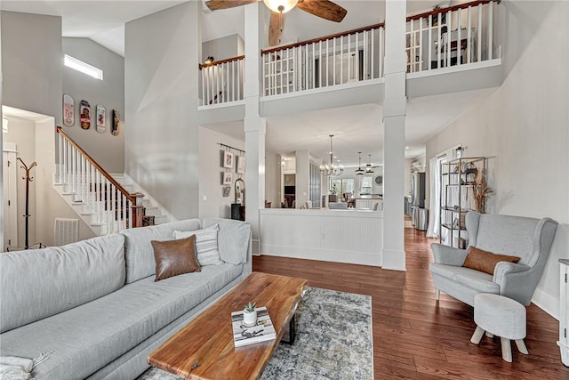 living room with ceiling fan with notable chandelier, wood-type flooring, a healthy amount of sunlight, and a high ceiling