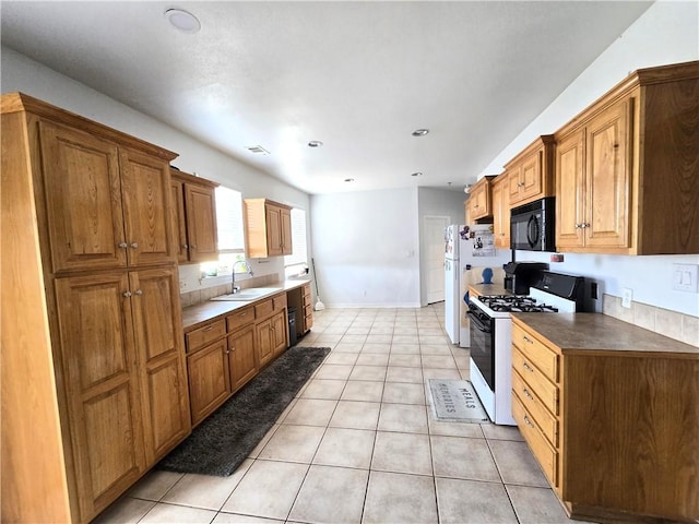 kitchen featuring light tile patterned flooring, sink, gas range oven, and white refrigerator