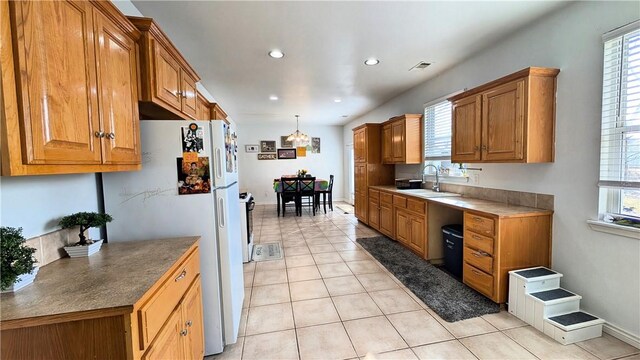 kitchen with sink, hanging light fixtures, white refrigerator, and light tile patterned floors