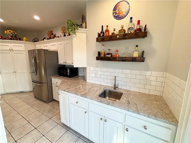 kitchen with sink, stainless steel fridge, white cabinetry, light stone counters, and light tile patterned flooring