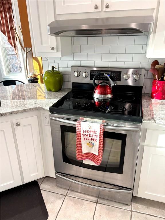 kitchen with stainless steel electric stove, white cabinetry, decorative backsplash, light tile patterned floors, and light stone counters