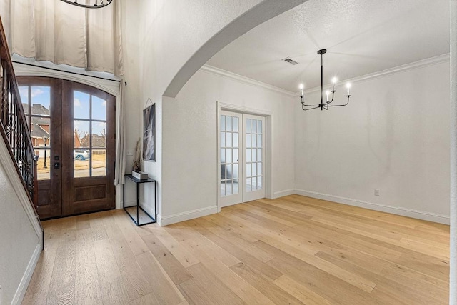 foyer entrance featuring an inviting chandelier, crown molding, light hardwood / wood-style floors, and french doors