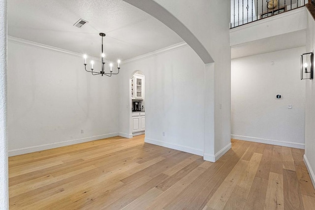 unfurnished dining area featuring an inviting chandelier, crown molding, and light hardwood / wood-style floors