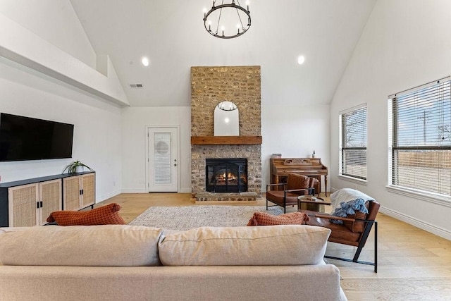 living room with an inviting chandelier, a large fireplace, high vaulted ceiling, and light wood-type flooring