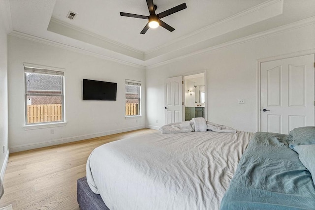 bedroom featuring ensuite bath, ornamental molding, light hardwood / wood-style floors, and a raised ceiling