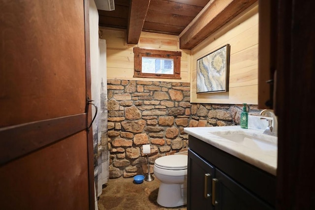 bathroom featuring beam ceiling, wooden walls, vanity, wooden ceiling, and toilet