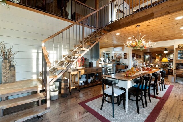 dining area with hardwood / wood-style flooring, a high ceiling, ceiling fan with notable chandelier, and wooden walls