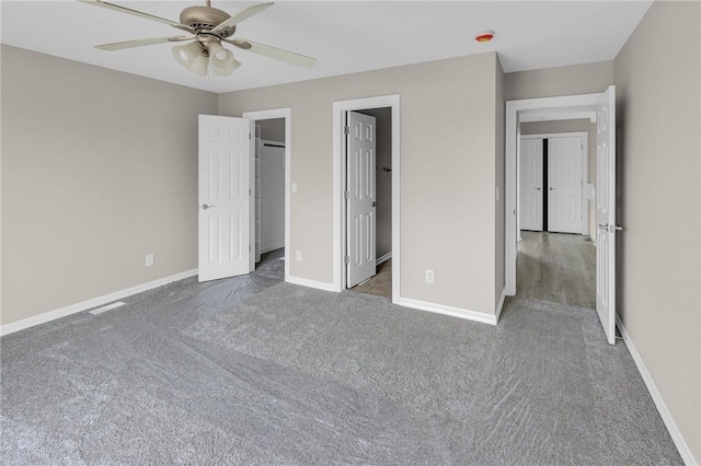 unfurnished bedroom featuring ceiling fan, a walk in closet, and dark carpet