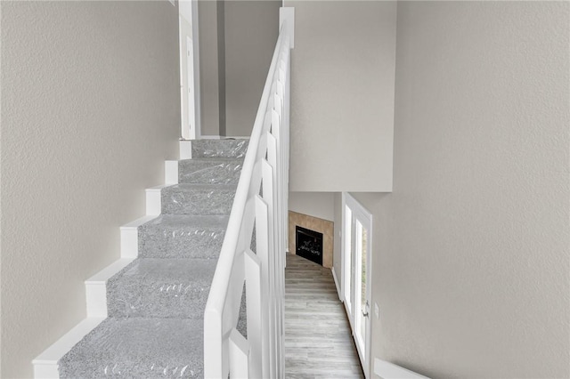 stairway with a tile fireplace and wood-type flooring