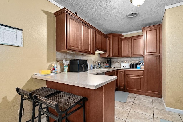 kitchen featuring light tile patterned flooring, sink, a kitchen breakfast bar, decorative backsplash, and kitchen peninsula