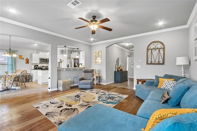 living room with crown molding, ceiling fan with notable chandelier, and light hardwood / wood-style flooring