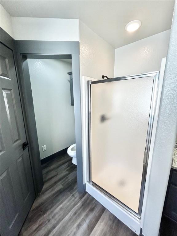 bathroom with toilet, a shower with door, and hardwood / wood-style floors