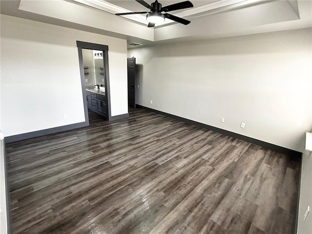 unfurnished bedroom featuring dark wood-type flooring, ensuite bath, and a raised ceiling