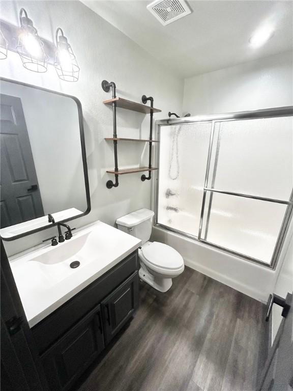 full bathroom featuring vanity, combined bath / shower with glass door, hardwood / wood-style floors, and toilet