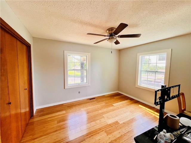 workout area with ceiling fan, a healthy amount of sunlight, light hardwood / wood-style flooring, and a textured ceiling