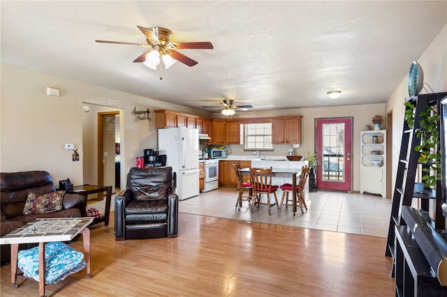 living room featuring sink, light hardwood / wood-style flooring, a textured ceiling, and ceiling fan