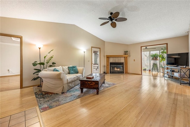 living room featuring lofted ceiling, a fireplace, light hardwood / wood-style flooring, and a textured ceiling