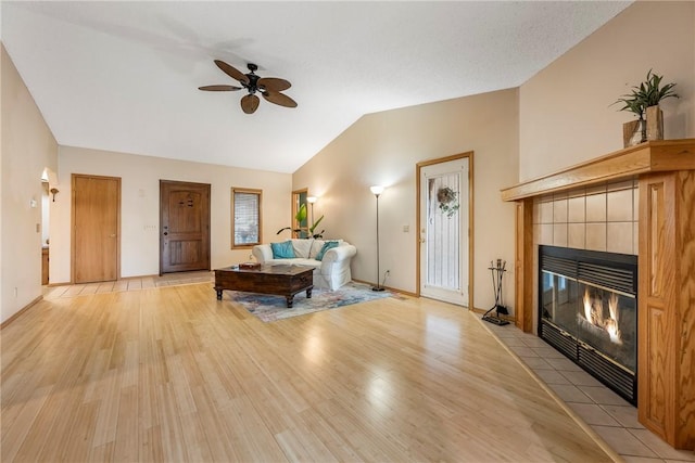 living room featuring vaulted ceiling, ceiling fan, a fireplace, and light hardwood / wood-style flooring