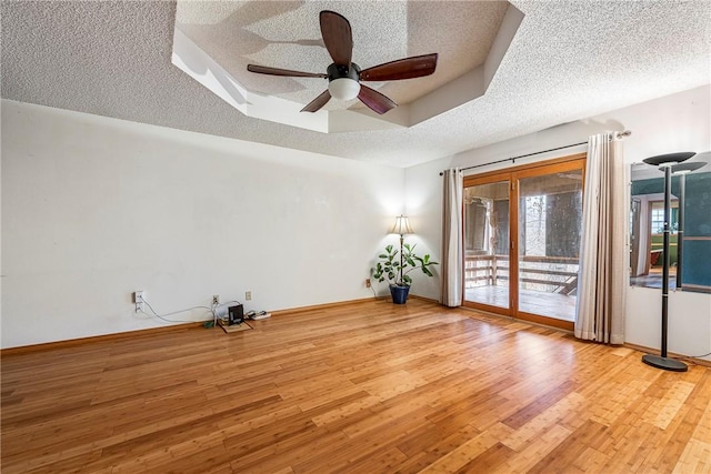 empty room with ceiling fan, a raised ceiling, light hardwood / wood-style floors, and a textured ceiling