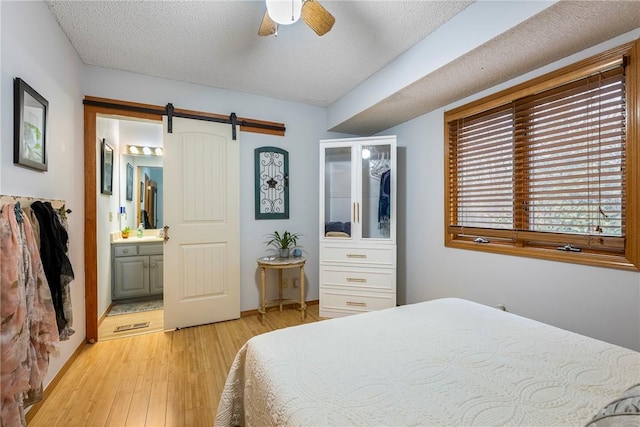 bedroom featuring ensuite bath, ceiling fan, light hardwood / wood-style floors, a textured ceiling, and a barn door