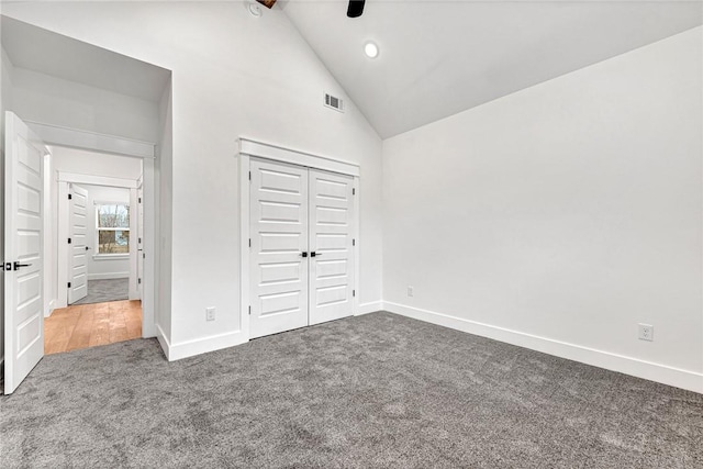 unfurnished bedroom with high vaulted ceiling, a closet, ceiling fan, and dark colored carpet