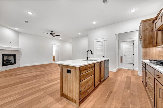 kitchen featuring appliances with stainless steel finishes, an island with sink, sink, ceiling fan, and light hardwood / wood-style flooring