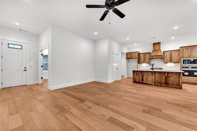 kitchen featuring built in microwave, stainless steel oven, custom exhaust hood, and light wood-type flooring