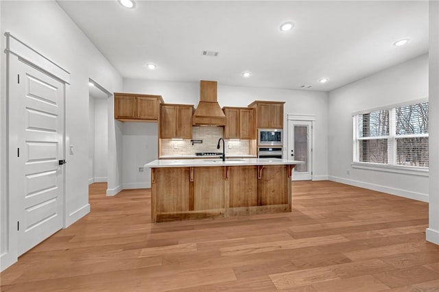 kitchen featuring sink, appliances with stainless steel finishes, a kitchen island with sink, decorative backsplash, and custom exhaust hood