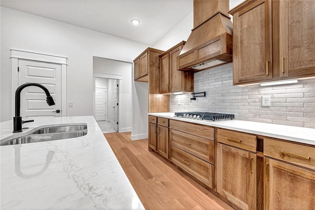 kitchen with sink, premium range hood, light hardwood / wood-style floors, stainless steel gas cooktop, and decorative backsplash