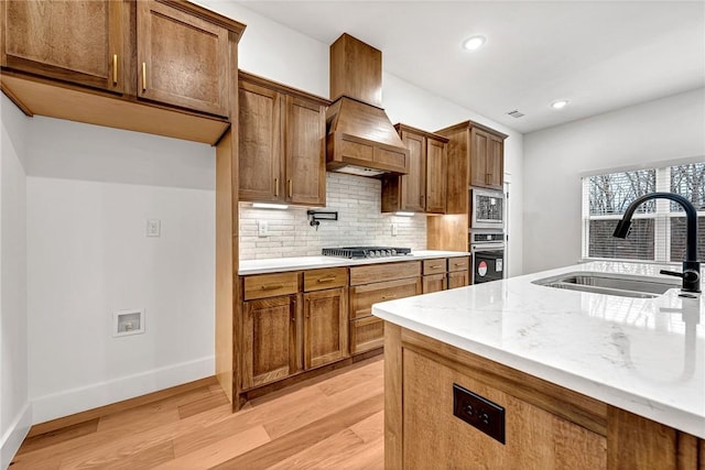 kitchen with sink, light stone counters, appliances with stainless steel finishes, light hardwood / wood-style floors, and decorative backsplash