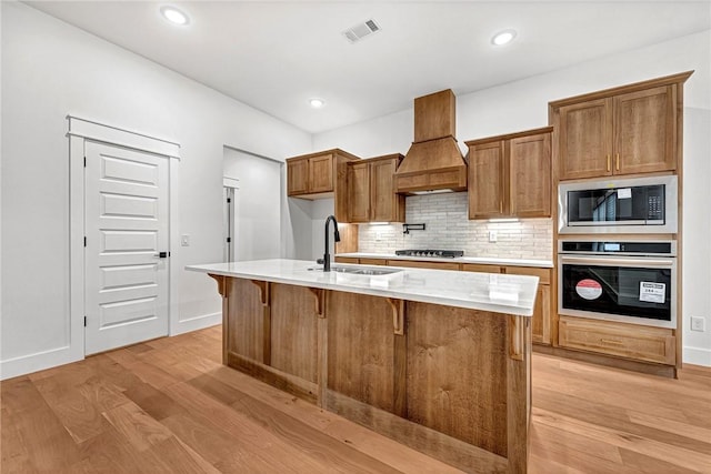 kitchen featuring an island with sink, appliances with stainless steel finishes, custom range hood, and sink