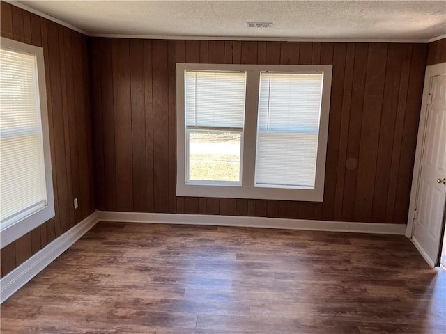 spare room with ornamental molding, dark hardwood / wood-style flooring, a textured ceiling, and wood walls