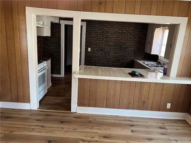 kitchen with dark wood-type flooring, sink, white gas stove, kitchen peninsula, and brick wall