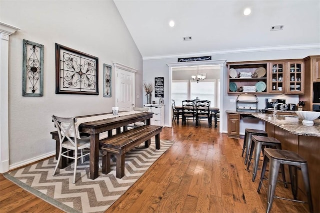 dining space with an inviting chandelier, high vaulted ceiling, dark wood-type flooring, and ornamental molding