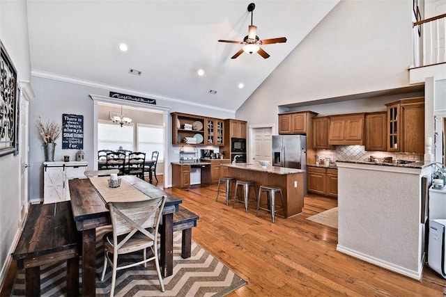 dining space featuring high vaulted ceiling, ceiling fan with notable chandelier, wood-type flooring, and ornamental molding