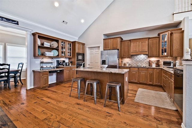 kitchen with a breakfast bar area, a center island, light stone countertops, black appliances, and ornamental molding