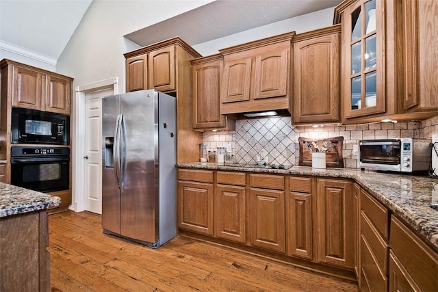 kitchen featuring lofted ceiling, black appliances, light hardwood / wood-style floors, and stone counters