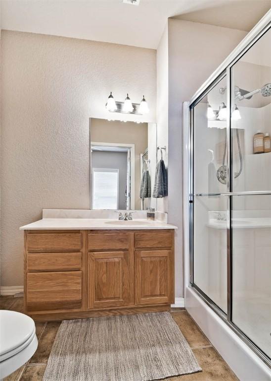 bathroom with a shower with door, vanity, tile patterned flooring, and toilet