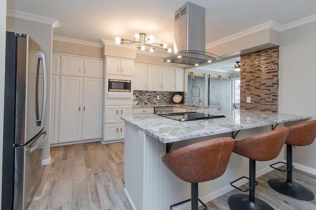 kitchen with island range hood, appliances with stainless steel finishes, kitchen peninsula, light stone countertops, and white cabinets