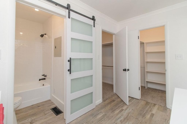 bathroom with hardwood / wood-style flooring, crown molding, tiled shower / bath combo, and toilet