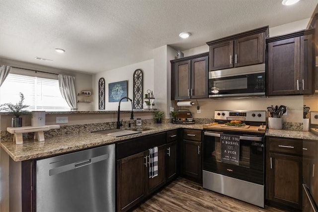 kitchen with light stone countertops, appliances with stainless steel finishes, sink, and kitchen peninsula